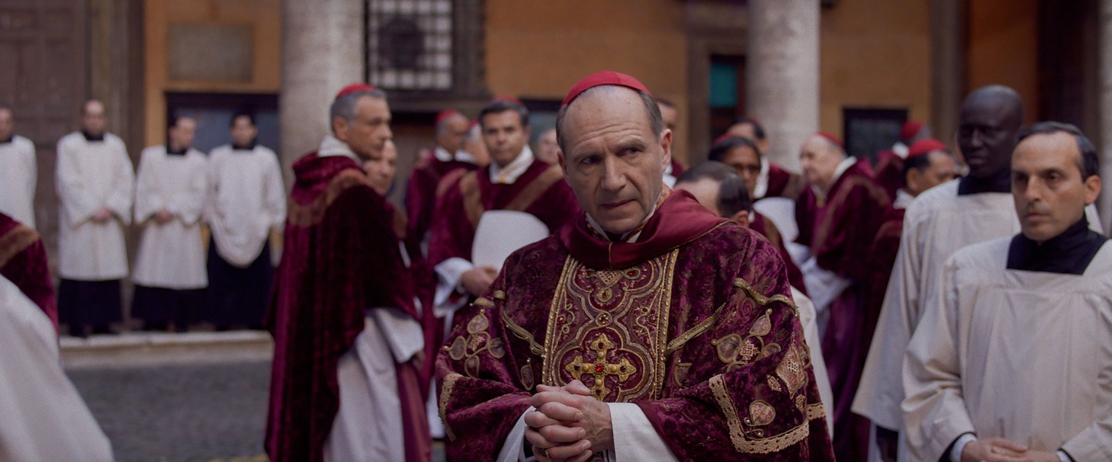 Still from Conclave showing cardinals in ceremonial robes gathered in a courtyard