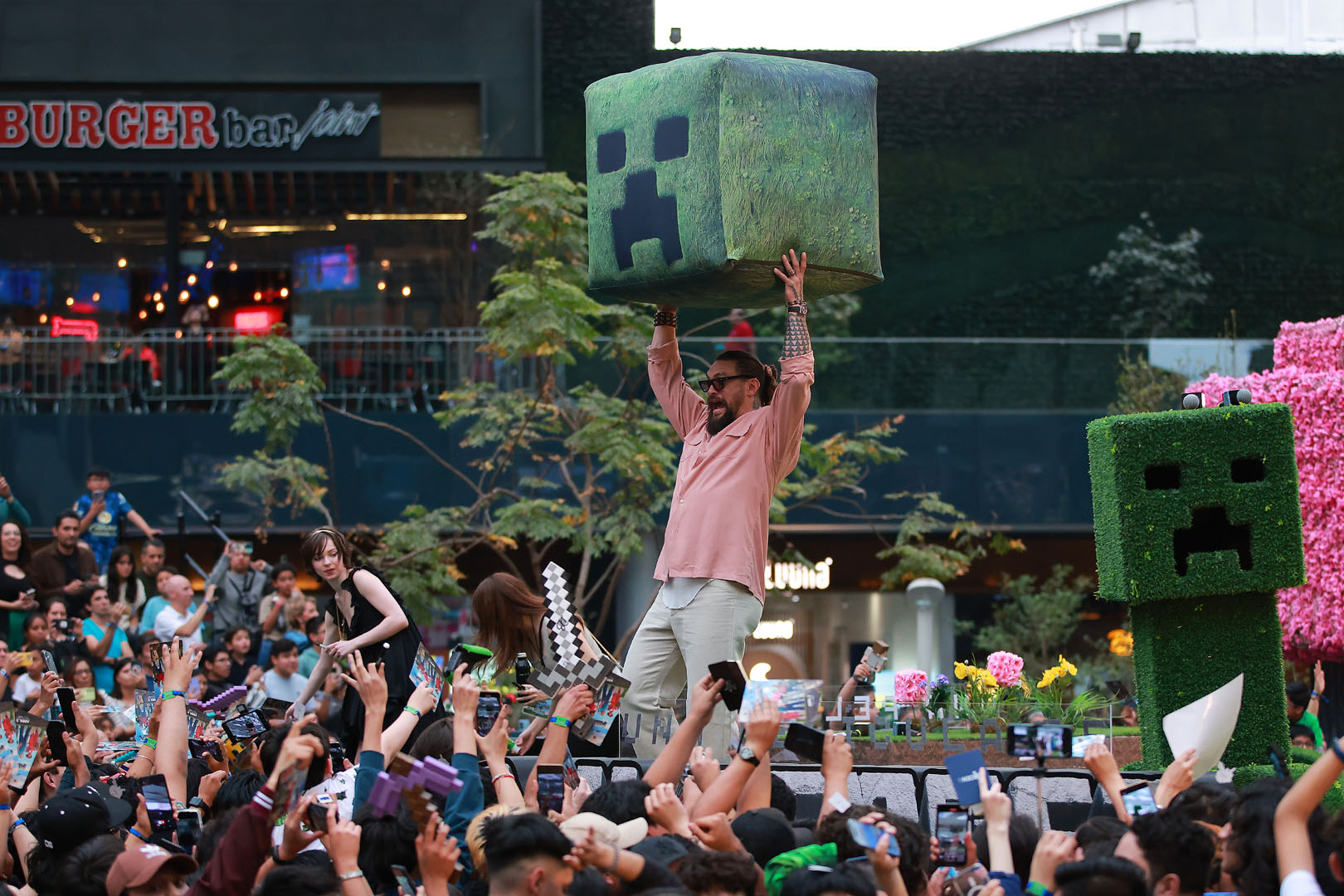 Jason Momoa promoting A Minecraft Movie, holding a large Creeper head prop