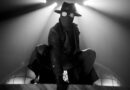 Masked figure as The Spider illuminated by dramatic spotlights in Spider-Noir