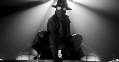 Masked figure as The Spider illuminated by dramatic spotlights in Spider-Noir