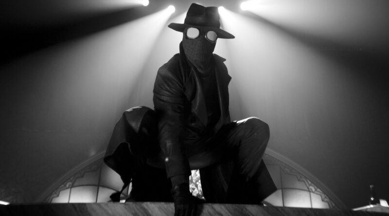 Masked figure as The Spider illuminated by dramatic spotlights in Spider-Noir