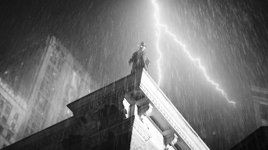 Silhouette of The Spider, played by Nicolas Cage, atop a building during a thunderstorm
