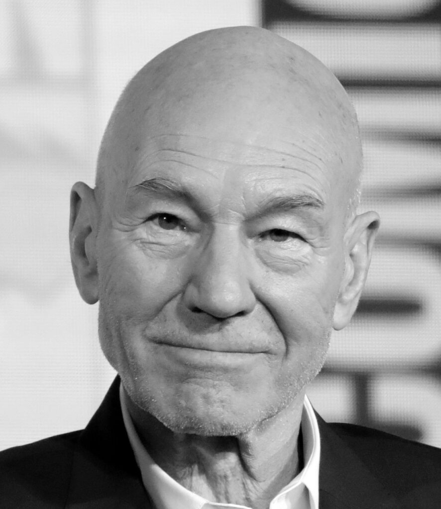 Close-up black-and-white portrait of Sir Patrick Stewart smiling softly at a 2019 panel