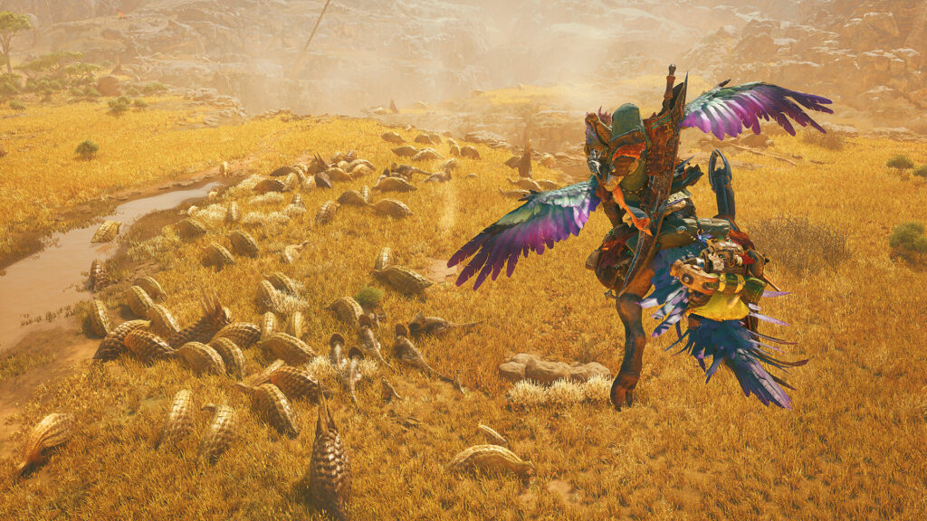 A hunter rides through golden grassland past a herd of armored creatures in Monster Hunter Wilds