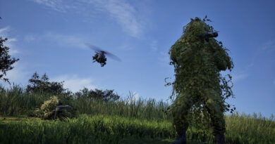 WARDOGS soldier in a ghillie suit watching a helicopter fly over a field