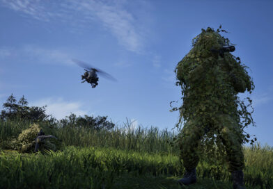 WARDOGS soldier in a ghillie suit watching a helicopter fly over a field