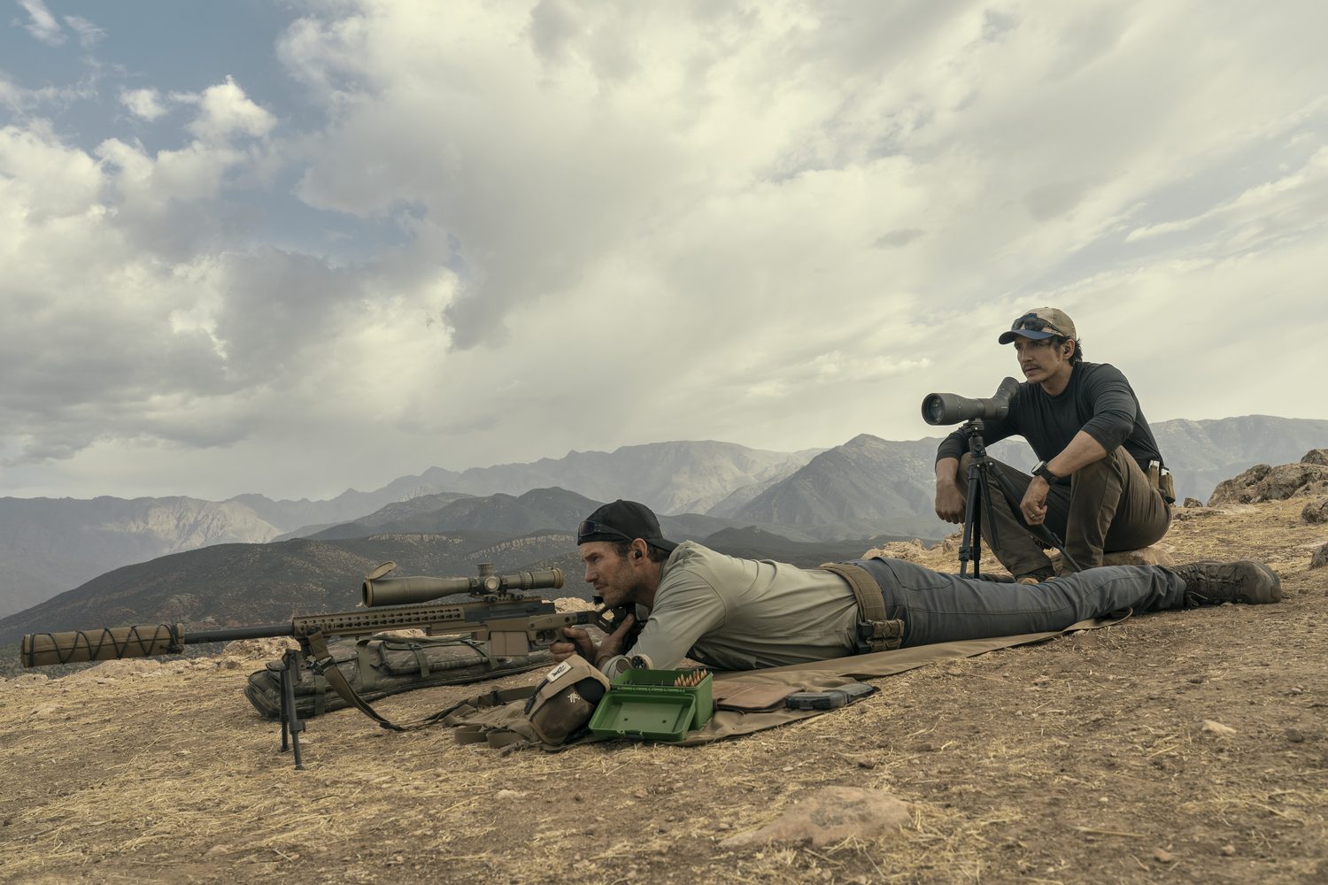 A sniper and a spotter lying on a rocky hillside above a mountain valley in The Terminal List Season 2